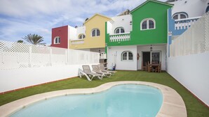 A pool area with a small patio and lounge chairs.