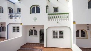 A white building with green trim, multiple windows, and a tiled courtyard.