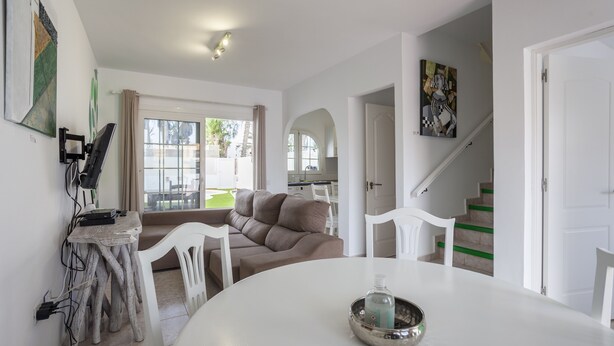 A modern living room with a round dining table, a sofa, and a staircase leading to an upper level.