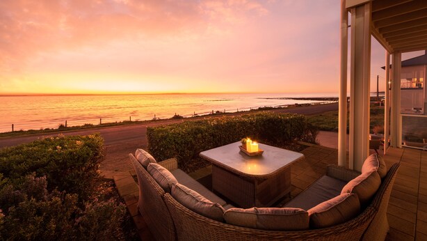 Eine Terrasse mit Korbmöbeln und einem Tisch, mit Blick auf einen Sonnenuntergang über dem Meer.