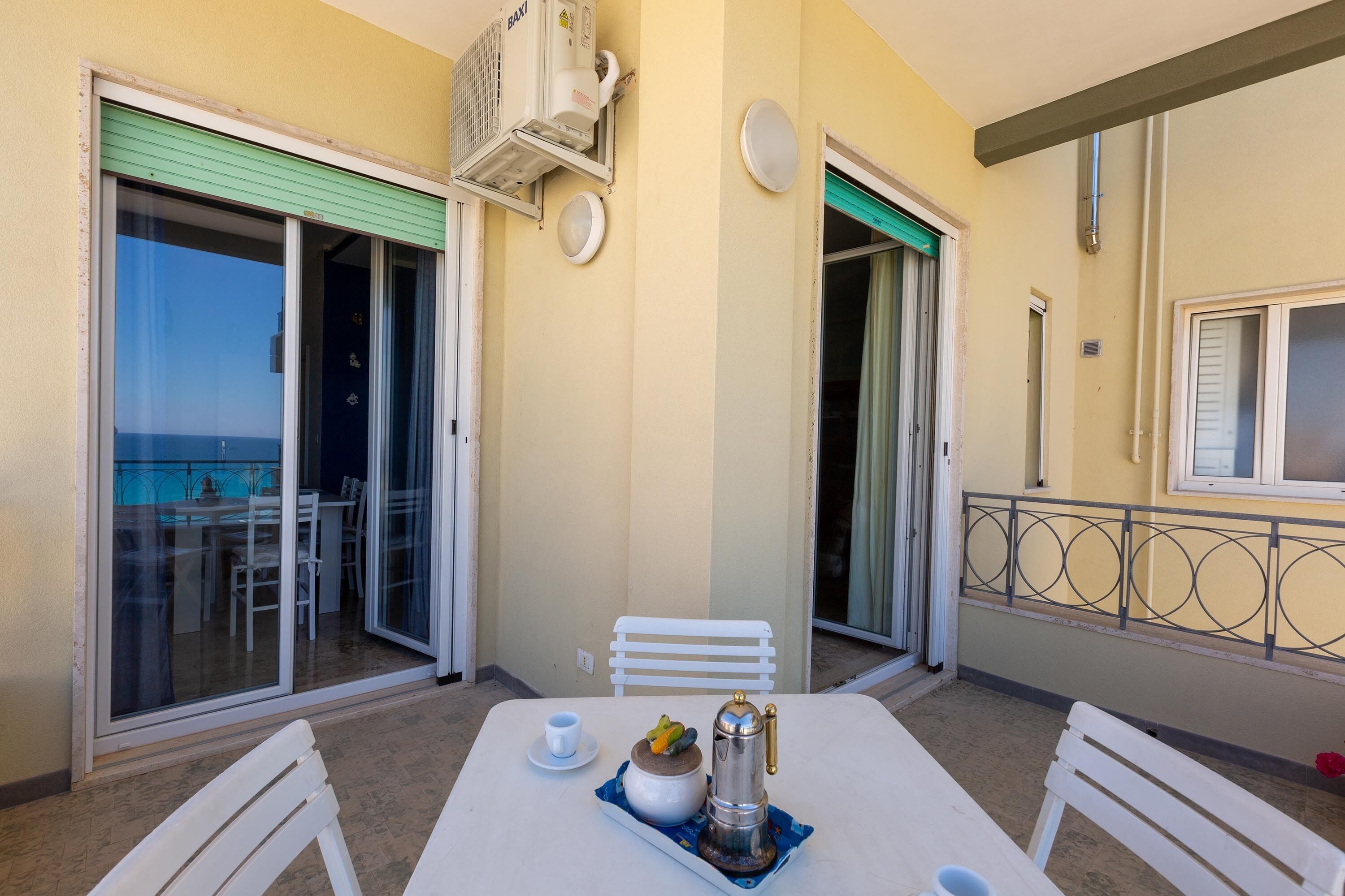 A balcony with a table set for two, a coffee pot, and a cup.