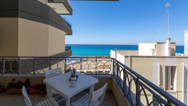 A balcony with a table and chairs, overlooking a beach and the sea. - 2419 Appartamento Kalepolis (Gallipoli)
