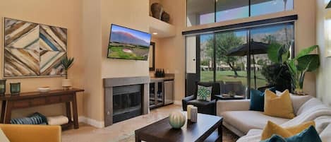 A spacious living room with a fireplace, comfortable seating, and large windows offering a view of the outdoors.