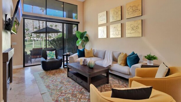 A spacious living room with a large window, a sofa set, a coffee table, and artwork on the wall. - Fabulously Remodeled 2 Bedroom Condo With Beautiful Golf and Mountain Views (La Quinta)