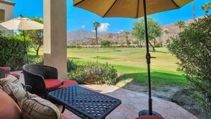 An outdoor patio with wicker furniture, a table, and an umbrella. - Fabulously Remodeled 2 Bedroom Condo With Beautiful Golf and Mountain Views (La Quinta)