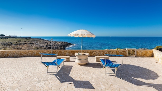 A patio with stone flooring, a white umbrella, and blue lounge chairs overlooking the sea. - 2696 Appartamento La Nave by Barbarhouse (Racale)