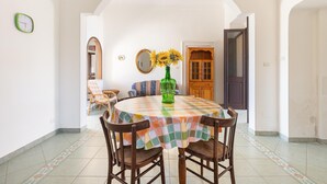 A dining area with a round table, chairs, a checkered tablecloth, a vase with sunflowers, a mirror, and a wooden door in the background. - 2696 Appartamento La Nave by Barbarhouse (Racale)