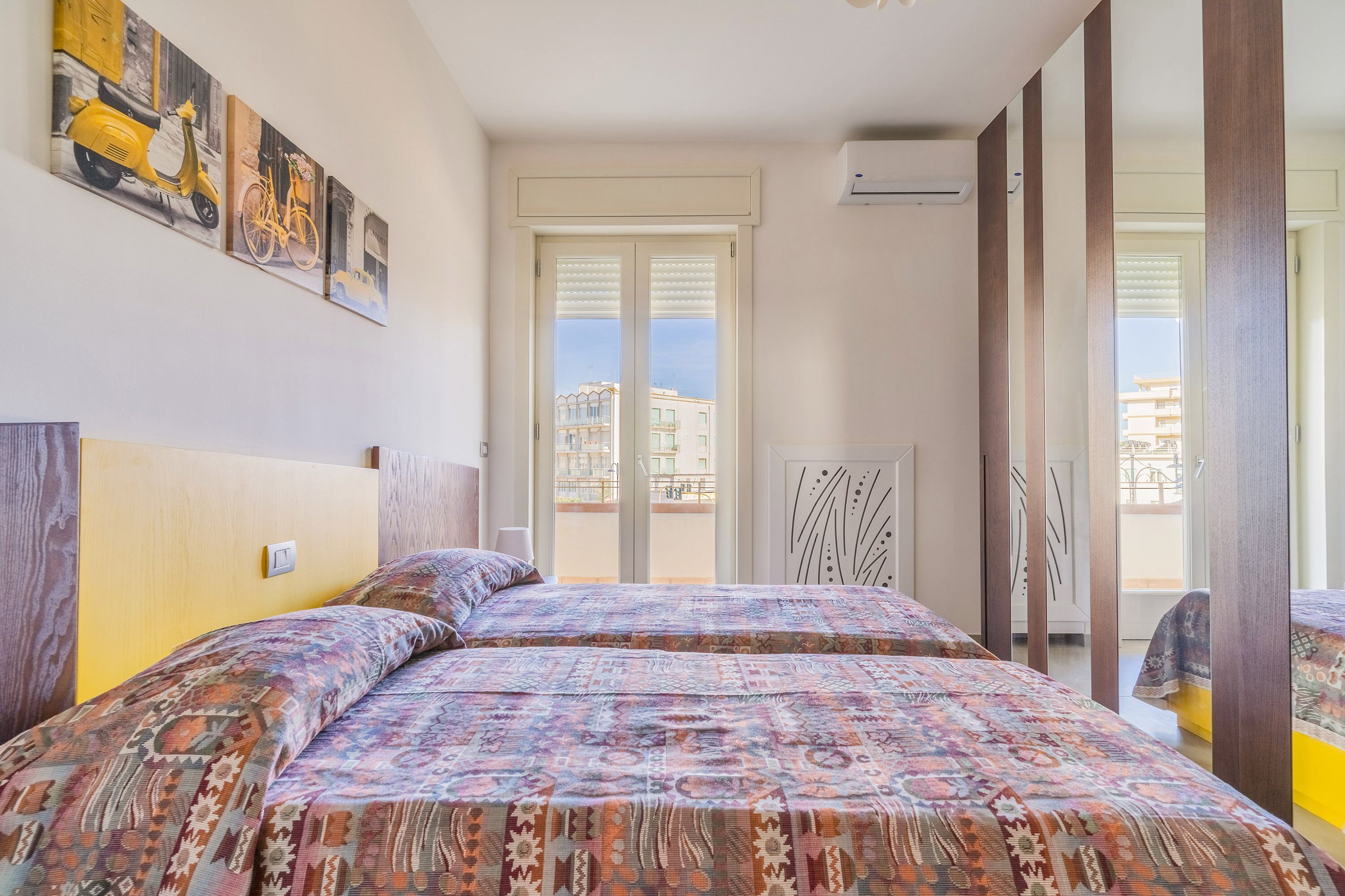 A bedroom with two beds, a window with blinds, a door, and a wall-mounted air conditioner.