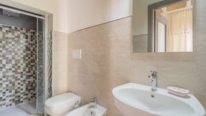 Een badkamer met een douche, toilet, bidet, wastafel en een spiegel.