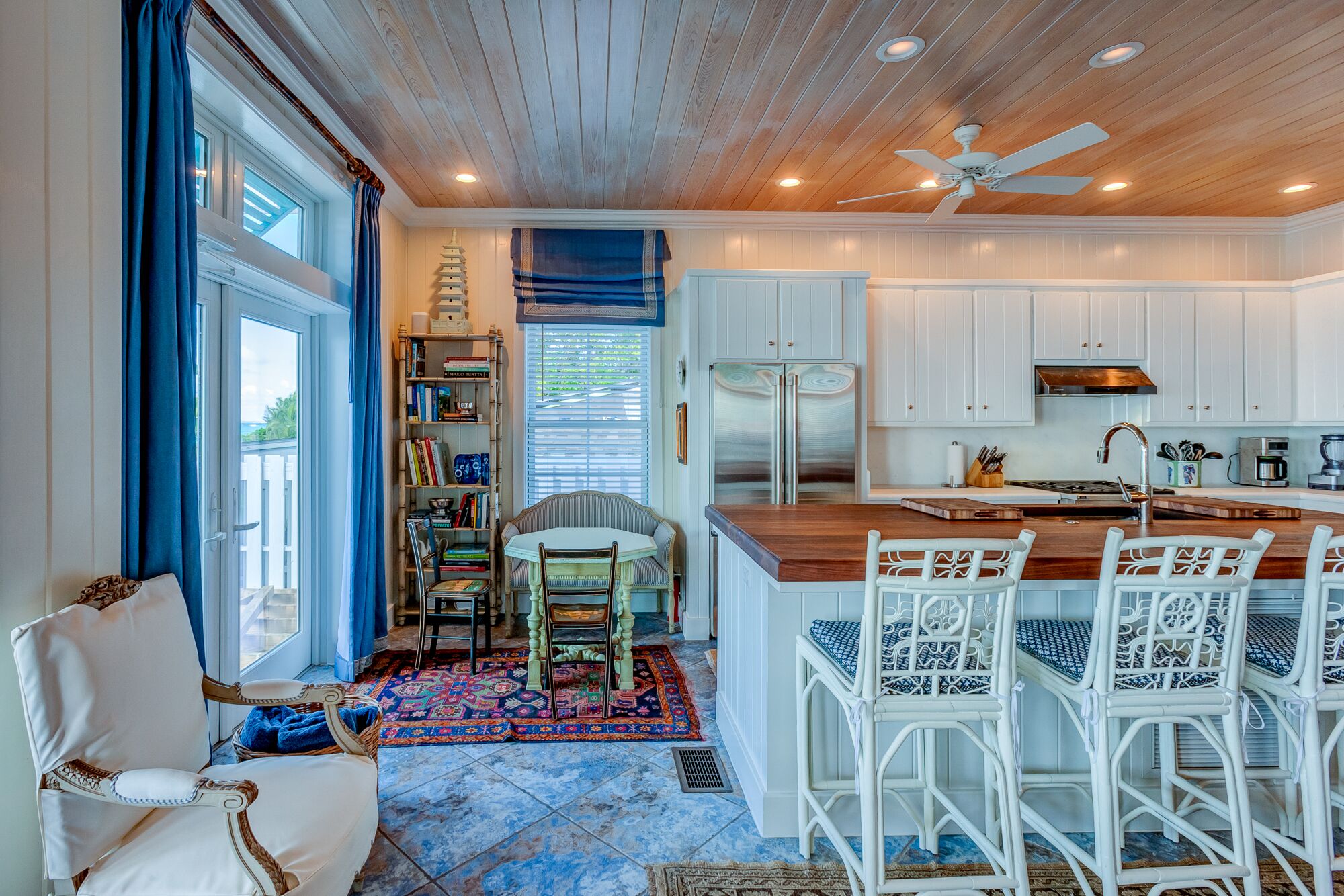 A spacious kitchen with white cabinetry, a wooden ceiling, and a central island with bar stools.