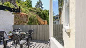 A deck with a table and chairs, a wooden fence, and a view of a hillside with trees. - Crew House (Dartmouth)