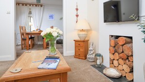 A living room with a wooden table, a TV mounted on the wall, and a fireplace with logs. - Crew House (Dartmouth)