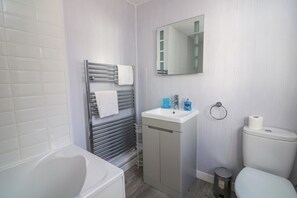 Un baño con una bañera blanca, un lavabo con un espejo encima y un inodoro.