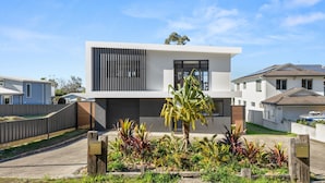 A modern two-story house with a flat roof, large windows, and a well-maintained garden with various plants. - Bella Vita by Experience Jervis Bay (Vincentia)