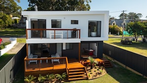 A modern two-story house with a balcony, outdoor seating area, and a garden. - Bella Vita by Experience Jervis Bay (Vincentia)