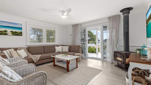 Ein modernes Wohnzimmer mit Sofa, Sesseln, einem Couchtisch, einem Kamin und Blick durch Glastüren.