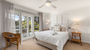 Ein Schlafzimmer mit einem großen Bett, einem Deckenventilator, einem Fenster mit Vorhängen und Blick auf Grün.
