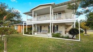 Ein zweistöckiges Haus mit Balkon, überdachter Veranda und gepflegtem Rasen.