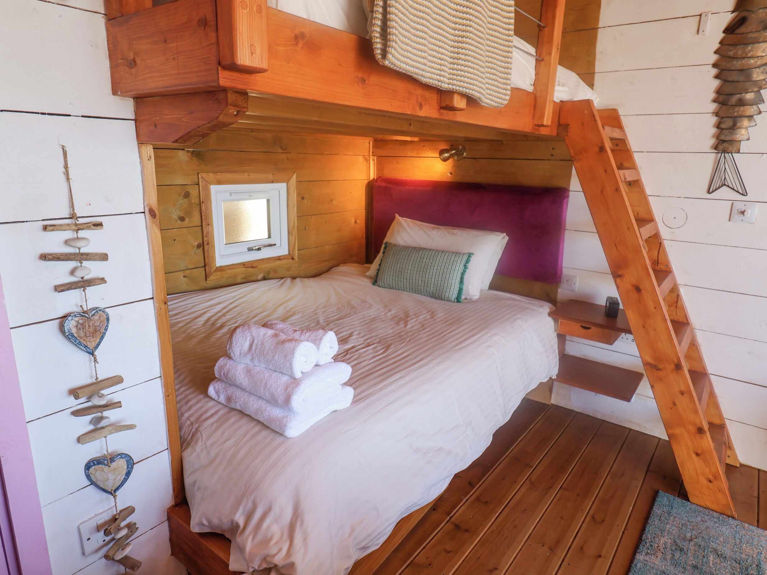 A cozy wooden cabin bedroom with a bunk bed, a heart-shaped wall decoration, and a ladder.
