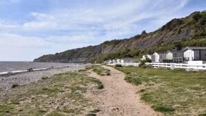 Un sentier côtier mène à une rangée de cabanes blanches, avec une plage rocheuse et une falaise en arrière-plan.