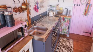 Une cuisine dotée d’un évier en acier inoxydable, d’une cuisinière rose et de divers ustensiles de cuisine accrochés au mur.