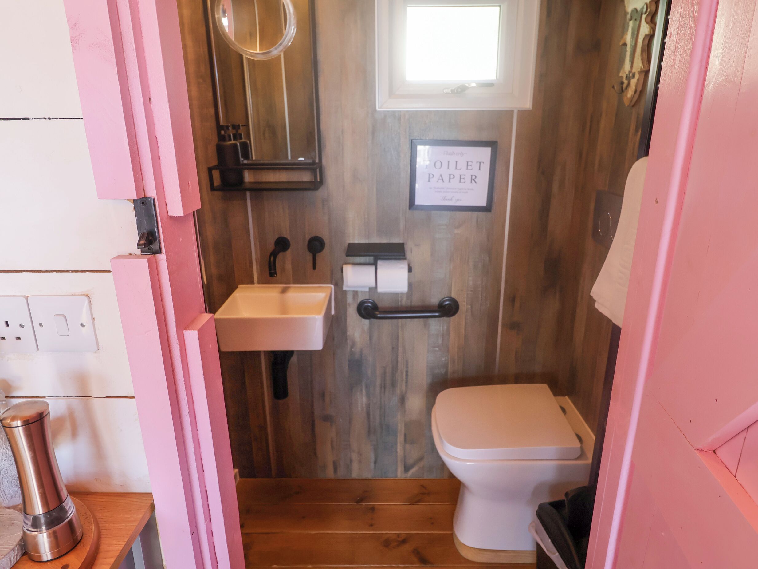 A compact bathroom with a wooden wall, a white sink, a toilet, and a small window.