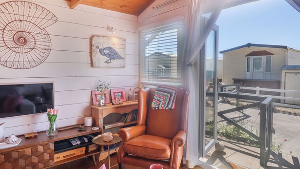 Un salon chaleureux avec un plafond en bois, une grande fenêtre donnant sur un quartier résidentiel, un téléviseur, un fauteuil en cuir confortable et une table basse en bois.