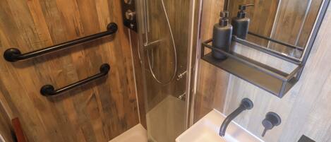 Un baño con pared de madera, cabina de ducha de vidrio, lavamanos blanco y espejo sobre el lavamanos.