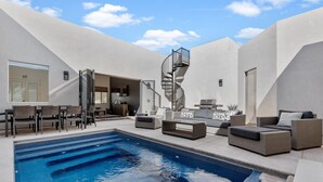 Uma área de piscina moderna ao ar livre, com escada em espiral, assentos e um bar.