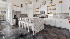 Cozinha moderna com armários brancos, bancada de granito e eletrodomésticos de aço inoxidável.