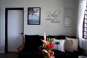 Ein Zimmer mit einem dunkelgrauen Sofa, einer Tür, einer Wand mit einem gerahmten Bild und einem dekorativen Schild.