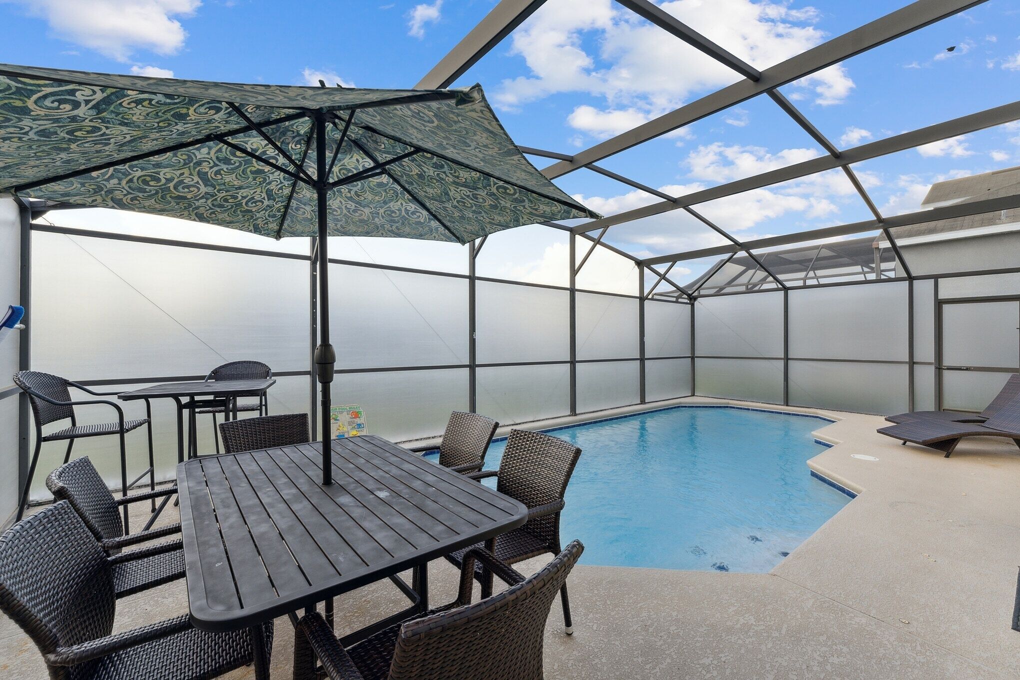 Un espace extérieur abrité avec une piscine, une table et des chaises, ainsi qu’un grand parasol.