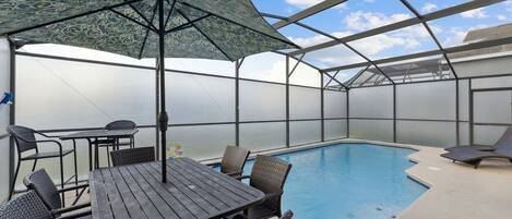 Un espace extérieur abrité avec une piscine, une table et des chaises, ainsi qu’un grand parasol.