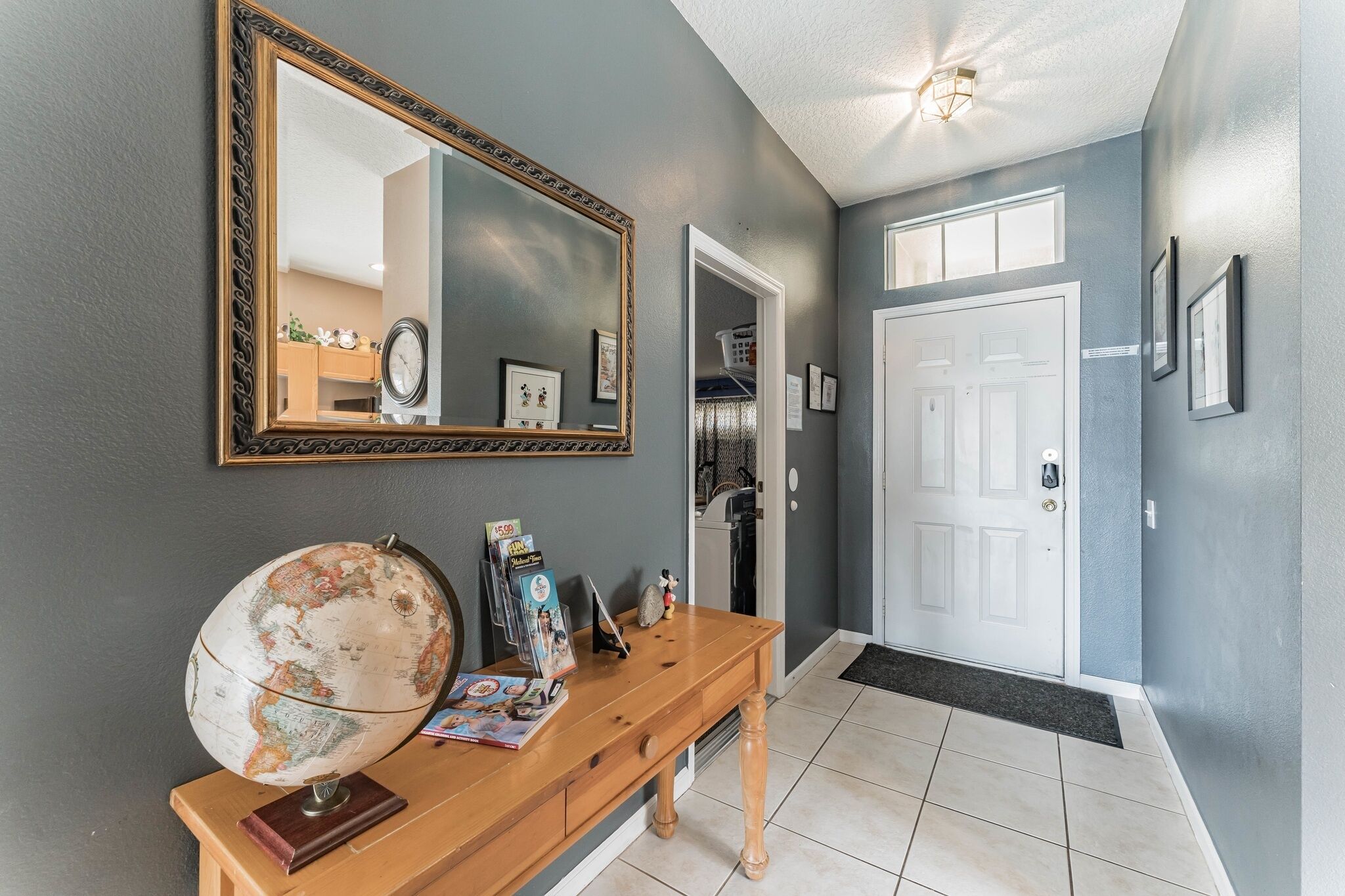 A hallway with a wooden console table, a globe, a mirror, and a door leading to a laundry room.