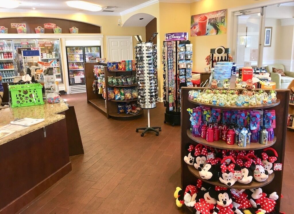 Un magasin avec des étagères remplies de jouets, un présentoir de poupées à l’effigie de Mickey Mouse et un réfrigérateur Coca-Cola.