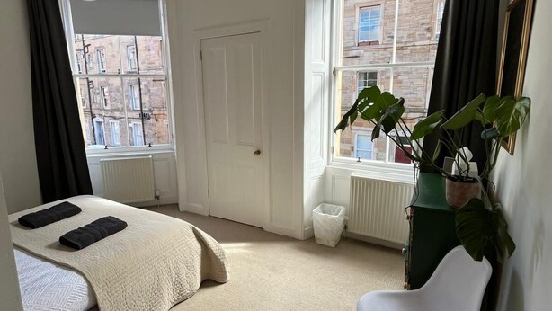 Un dormitorio con cama, una silla, una planta en maceta y un radiador.