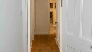 Un pasillo estrecho con suelo de madera y paredes blancas, que conduce a una puerta con un escalón en la entrada.