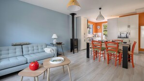 Ein modernes Wohnzimmer mit einer Couch, einem Holztisch mit einem roten Apfel und einer Küchenzeile mit einem Esstisch und Stühlen.