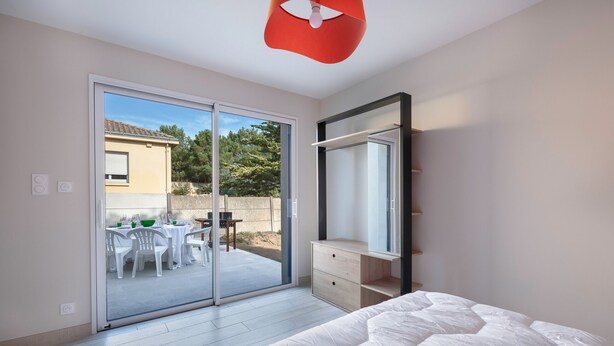 Ein Schlafzimmer mit einem großen Bett, einer Schiebetür zu einer Terrasse mit Tischen und Stühlen sowie einem Einbauschrank.