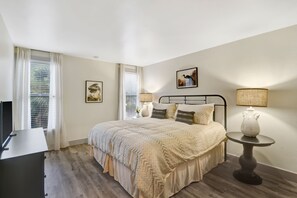 A bedroom with a bed, two bedside lamps, a small table, and a TV. - Newly Remodeled! Short Walk to Beach and Coligny (Hilton Head Island)