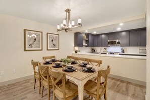 A dining area with a wooden table set for six, surrounded by wooden chairs. A chandelier hangs above, and there are two framed bird paintings on the wall. - Newly Remodeled! Short Walk to Beach and Coligny (Hilton Head Island)