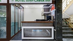 Uma mesa de recepção com divisória de vidro identificada com a palavra 'RECEPTION' e uma placa acima com a inscrição 'HOTEL MVP Check Inn'.
