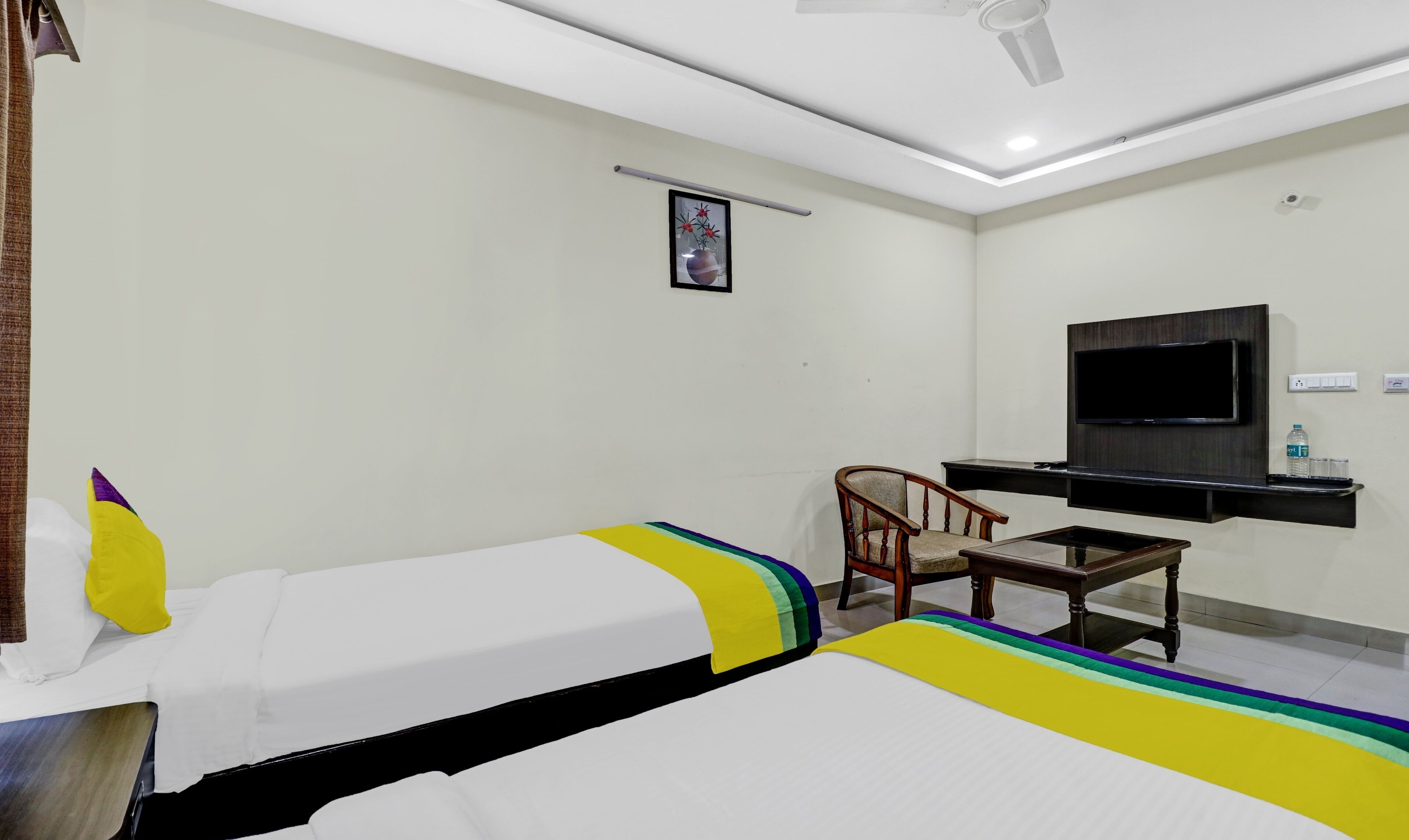 Habitación de hotel con dos camas, un escritorio, una silla, un televisor y un ventilador de techo.