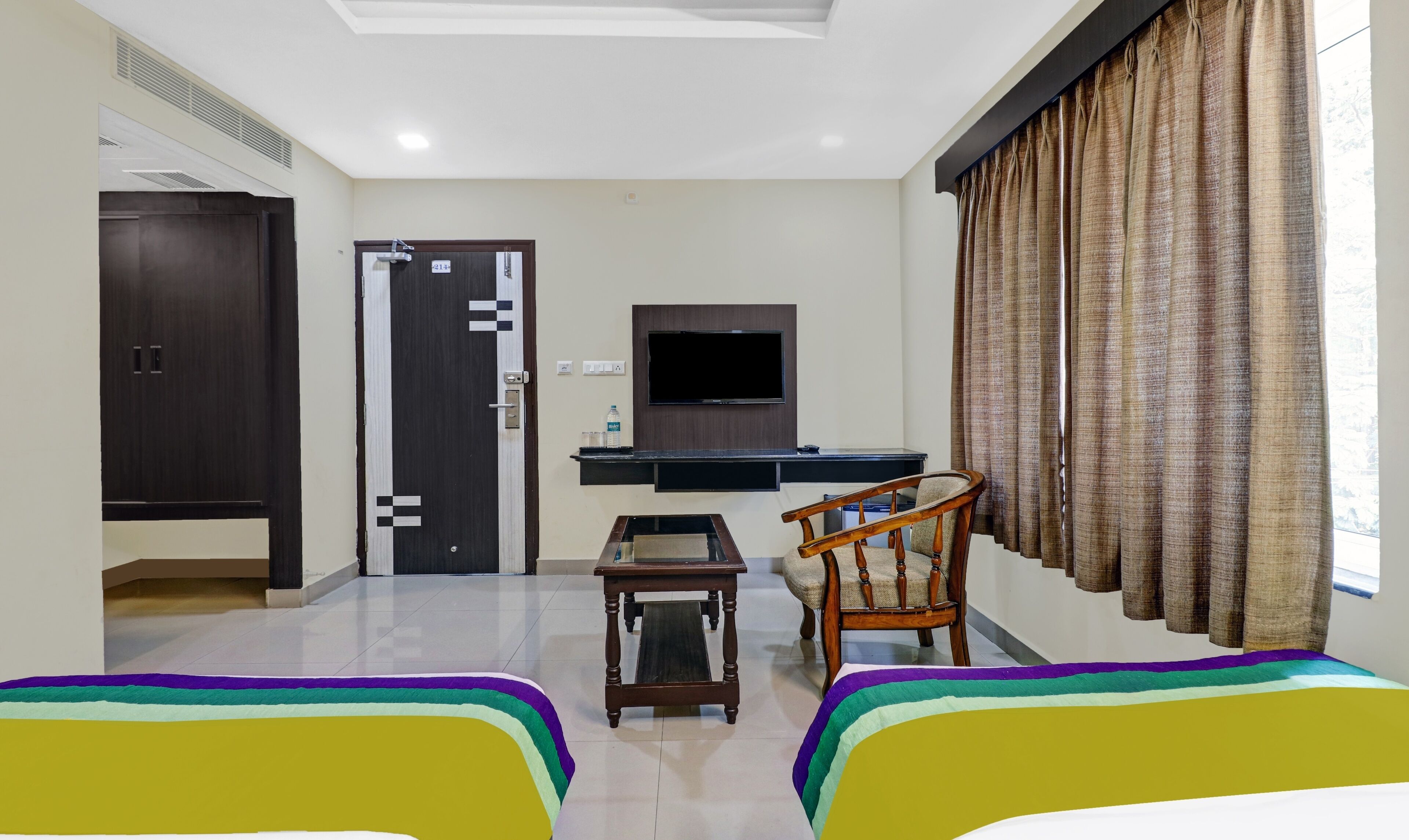 A hotel room with a bed, a desk, a chair, a television, and a wardrobe.