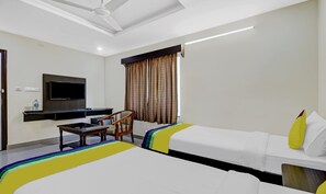 Une chambre d’hôtel avec deux lits, un bureau, une chaise, un téléviseur à écran plat et un ventilateur de plafond.