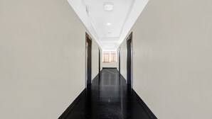 Um corredor comprido e estreito com pisos de mármore preto e paredes brancas, que dá para um quarto com janela e cortinas.