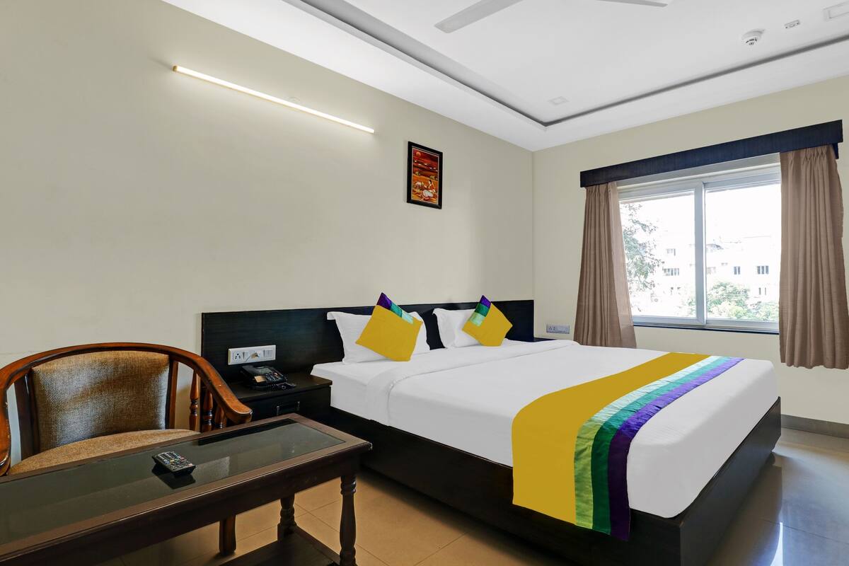 A hotel room with a bed, bedside table, chair, and a window with curtains.