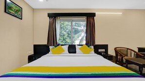 Quarto de hotel com uma cama grande, uma mesa de cabeceira, uma cadeira e uma janela com cortinas.