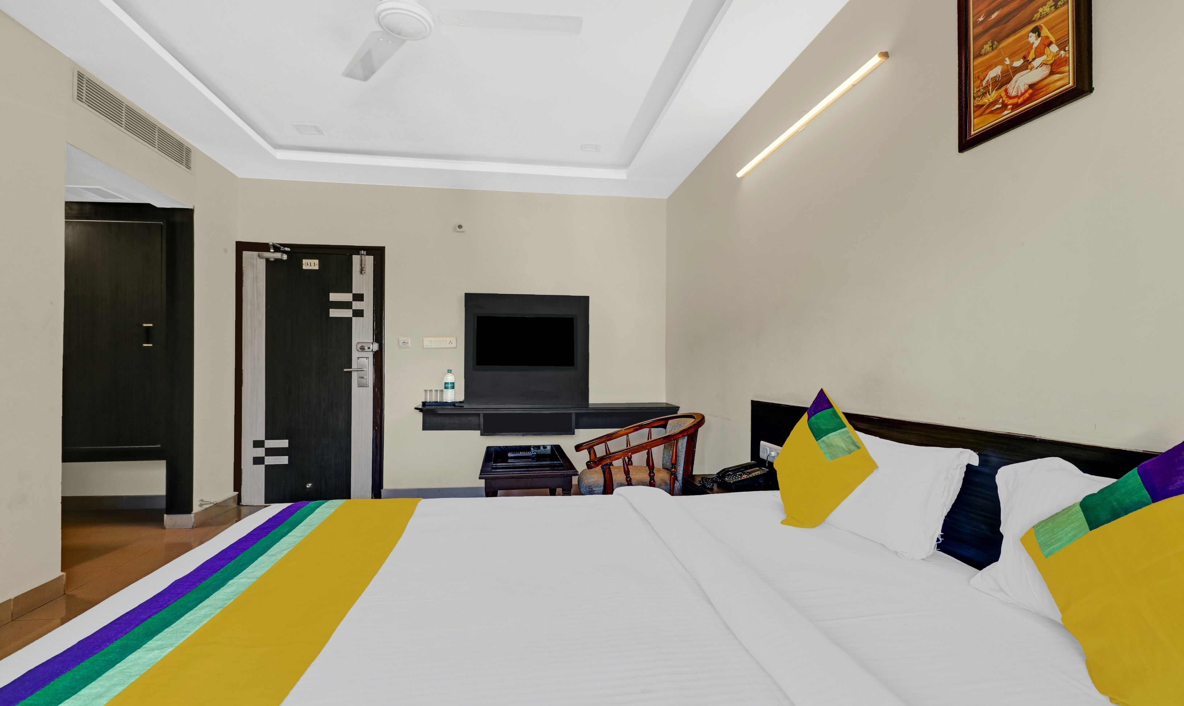 Habitación de hotel con una cama grande, un televisor de pantalla plana en la pared, un escritorio con una silla y un ventilador de techo.