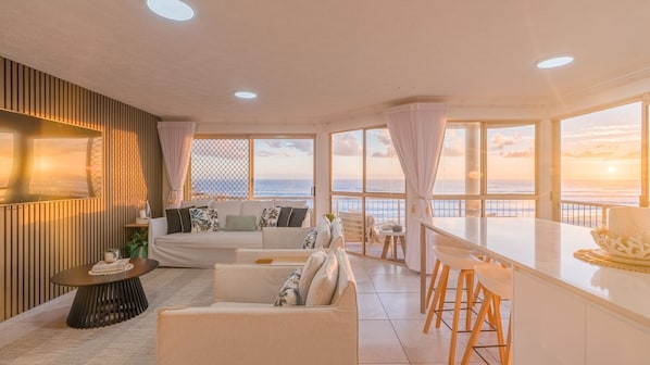 A spacious living area with a sofa, chairs, a dining table, and a view of the ocean.